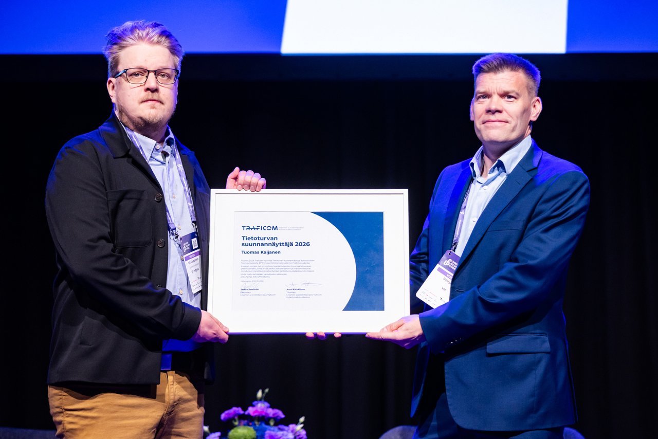 Kaksi miestä seisovat lavalla katsoen kameraan ja pitävät välissään kehystettyä diplomia.