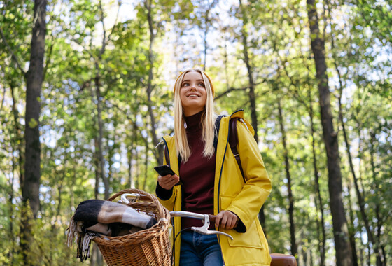 Nuori nainen seisoo metsässä pyörän vieressä kännykkä kädessä.