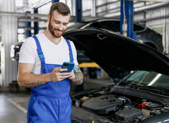 Nuori mies kännykän kanssa autokorjaamossa