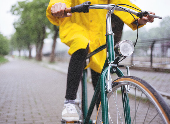 Pyöräilijä pyöräilemässä keltaisessa sadetakissa