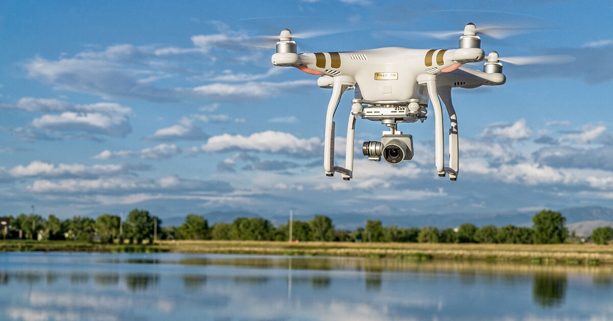 Valkoinen drone lentämässä, taustalla vesistöä